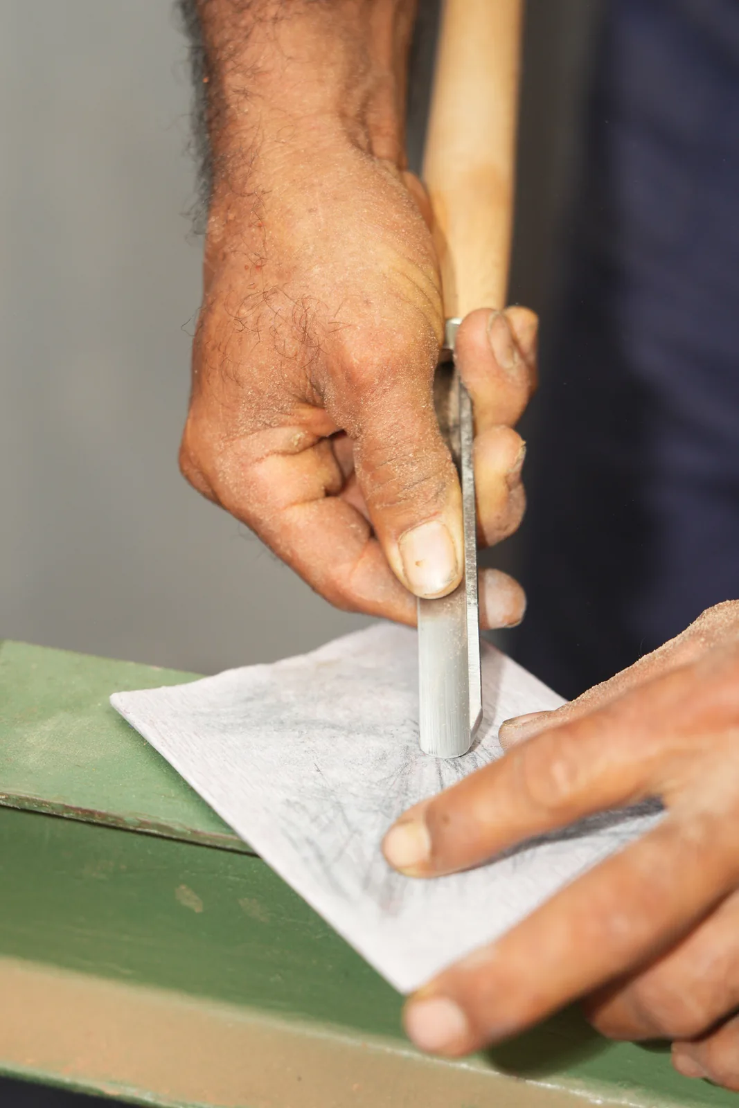 Manos sosteniendo un formón sobre un plano dibujado a lápiz en papel, apoyado en el banco de trabajo