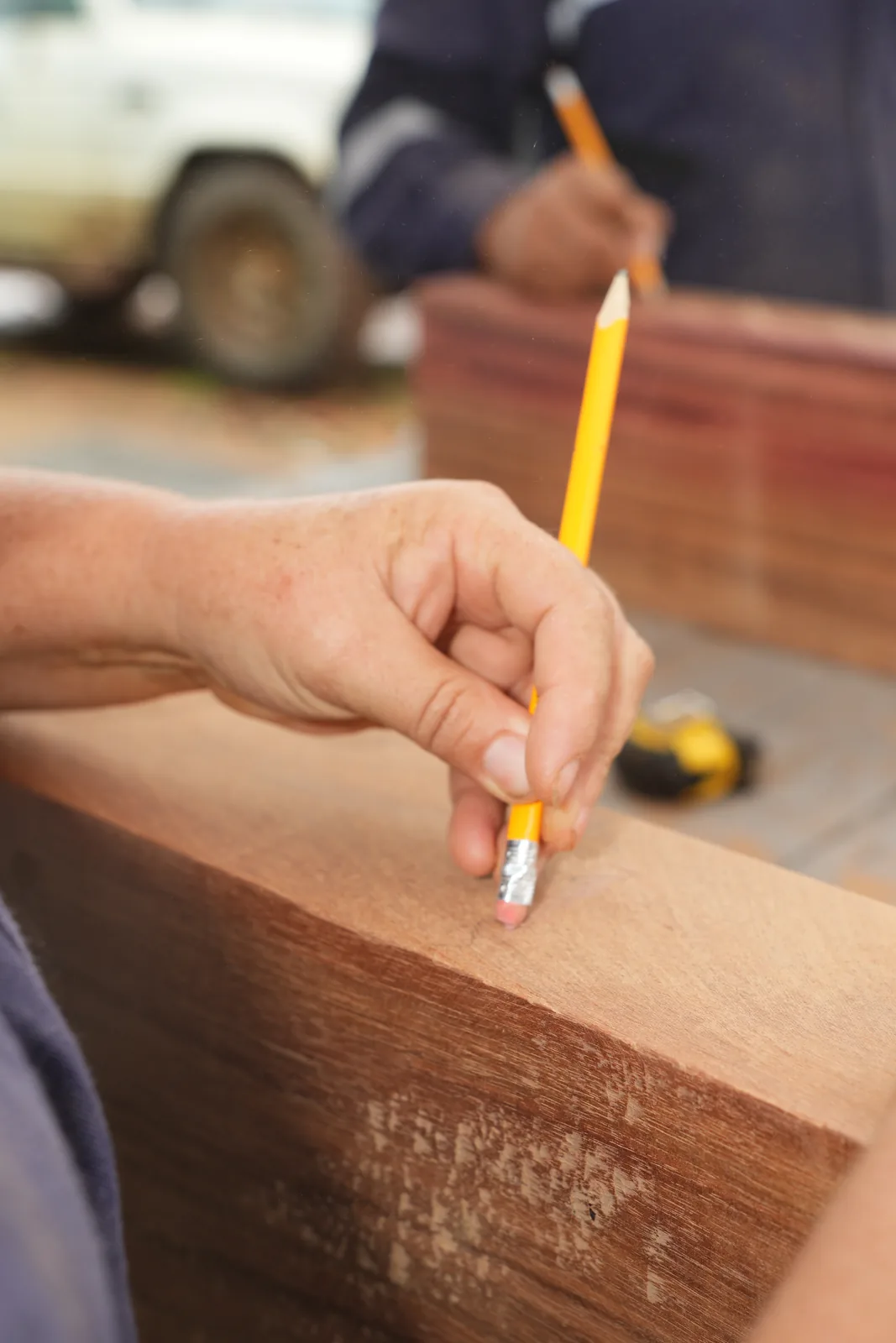 Primer plano de una mano marcando con lápiz amarillo una línea sobre el canto de una tabla de madera rojiza