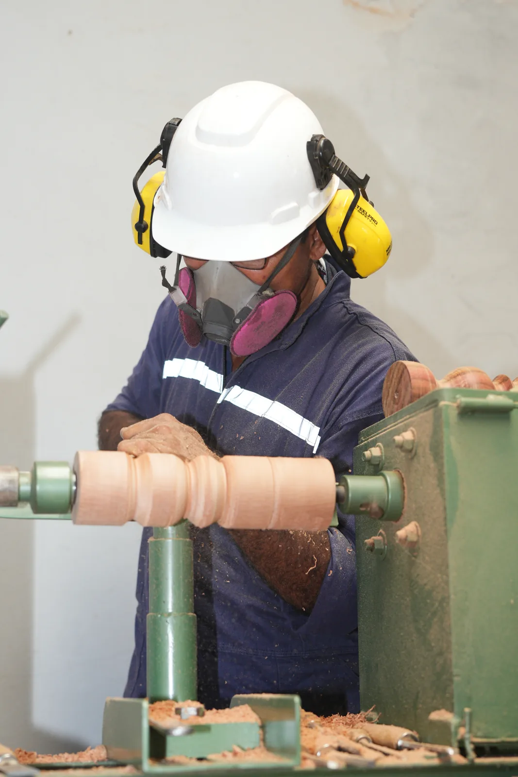 Ebanista trabaja en el torno de madera dando forma a un balaustre; las virutas se acumulan sobre la bancada verde